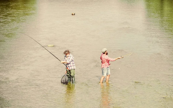 ゲームをしろ。レクリエーションやレジャーの屋外。大きなゲーム釣り。男性の友情。釣竿と網を持った2人の幸せな漁師。趣味とスポーツ活動。トラウト・ベイト。父と息子の釣り。冒険 — ストック写真