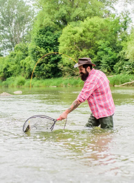 Guida sull'acqua verde. uomo maturo pesca a mosca. uomo cattura il pesce. hobby e attività sportive. Pothunter. pescatore con canna da pesca. weekend estivo. Pesca d'altura. pescatore barbuto in acqua — Foto Stock