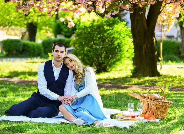 Picknicken in het stadspark. Man en vrouw ontspannen met de voedselmand. Romantisch reiziger paar onder sakura bloesem boom. Verliefd stel op groen gras. samen genieten van de natuur — Stockfoto