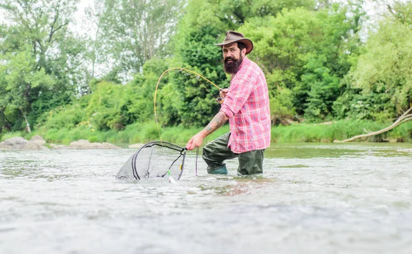 Fishing is astonishing accessible recreational outdoor sport. Fishing provides that connection with whole living world. Find peace of mind. Fishing hobby. Bearded fisher catching trout fish with net — Stock Photo, Image