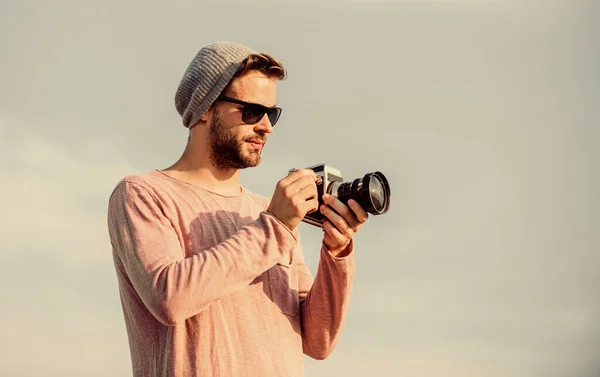 Concepto de fotoperiodista. Guy fotógrafo al aire libre cielo fondo. Hipster reportero tomando fotos. Configuración manual. Blogger de viajes. Fotógrafo profesional. Hermoso fotógrafo chico cámara retro — Foto de Stock