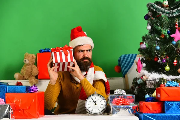 산타가 선물 상자를 들고 있어. 수염을 기르고 호기심많은 얼굴을 한 남자 — 스톡 사진