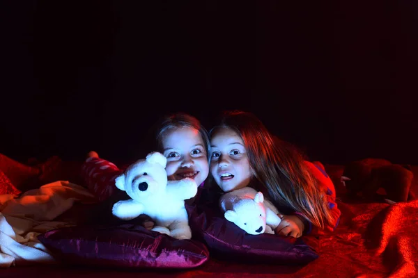 Les enfants en pyjama se couchent avec des ours en peluche sur fond sombre. — Photo