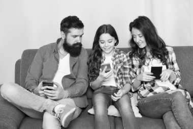 Oyun uygulaması oynat. Çevrimiçi aile. Anne baba ve kızı kanepede dinleniyor. Aile hafta sonunu internette geçiriyor. Küçük bir kız çocuğu, ailesine karşı akıllı telefon kullanıyor. İnternette aile sörfü. Aile eğlencesi.