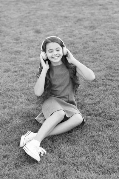 Moja letnia playlista. Słuchaj muzyki podczas relaksu na świeżym powietrzu. Podcast edukacyjny. Dziewczynka cieszyć się muzyką zielonej trawy łąki. Przyjemny czas. Słuchawki dla dzieci słuchają muzyki. Dziewczęce słuchawki słuchające muzyki — Zdjęcie stockowe