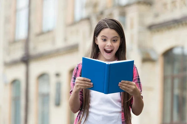 Ontdek iets nieuws. Gelukkig kind leest boek buiten. Opgewonden boekenwurm met open mond. Schoolbibliotheek. Literatuur lezen. Geletterdheid onderwijs. Kinderboek. Boekverhaal. Het boek oclock — Stockfoto