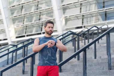 Büyük ilerleme. Formda ve sağlıklı kalmak. Sabah koşudayken saatini kontrol ediyor. Akıllı saati olan koşan bir adam. Akıllı saat kullanan yakışıklı fitness adamı. Aletlere bakan kaslı sporcu