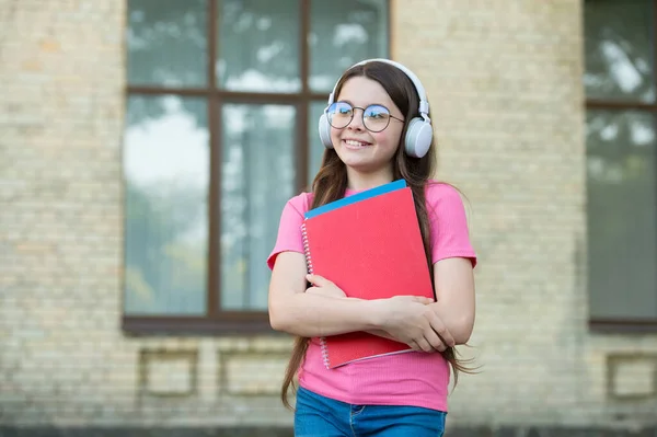 女の子は世界に値する。電子ブックから知識を得る。近代的な学校教育。学校に戻って。ハッピーティーンはワークブックを運ぶ。笑顔の子供はフォルダを保持します。子供の頃の幸せ。ヘッドセットの女の子は音楽を聞く — ストック写真