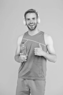 İçme suyu. Neşeli atletik adam müzik dinliyor. Vücudunu ve zihnini formda tut. Mutlu sporcu su şişesini tutuyor. Spor hocası. Susuzluk hissediyorum. Susuzluk ve susuzluk. Susuzluk kontrolü