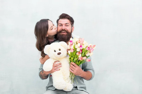 Father I love you. Happy daughter kiss father. Bearded man and little child hold flowers and toy. Happy family celebrate holiday. Love and care. Birthday anniversary. Fathers day. Congratulations