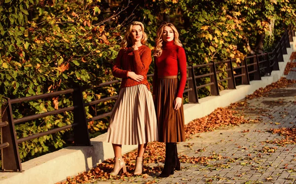 Fall fashion. Pleated skirt fashion trend. Women walking in autumn park. Autumn stylish outfit. Adorable ladies enjoy sunny autumn day. Fashionable clothes. Femininity and tenderness. Friends girls