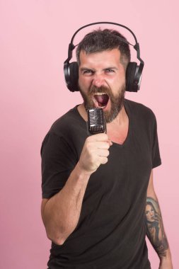 Adam pembe arka planda şarkı söylüyor. Sakallı DJ kulaklık takıyor..