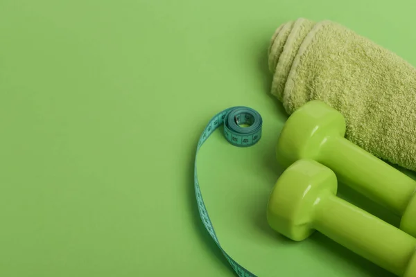 Dumbbells in bright green color, twisted measure tape and towel