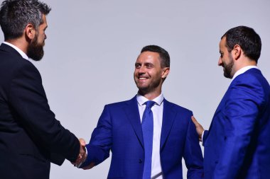 Gri arka planda resmi giyinmiş gülen yüzlü iş adamları.