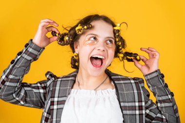 Sarı arka planda saç tokası ve saç tokası olan bir kız. Saçlarının etrafında kıvırcık kızlar. Güzel bir saç stili yap. Harika bir saç stili. Mutlu çocuk. Kuaför salonu. Mükemmel güzellik