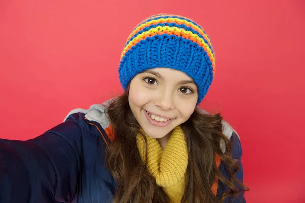 Selfiekamera. Le sött ansikte. Liten flicka bär vinterkläder röd bakgrund. Barndomskoncept. Känslomässig flicka långt hår stickad hatt. Tonårstjej avslappnad stil. Känslor och humör. Personlig blogg — Stockfoto