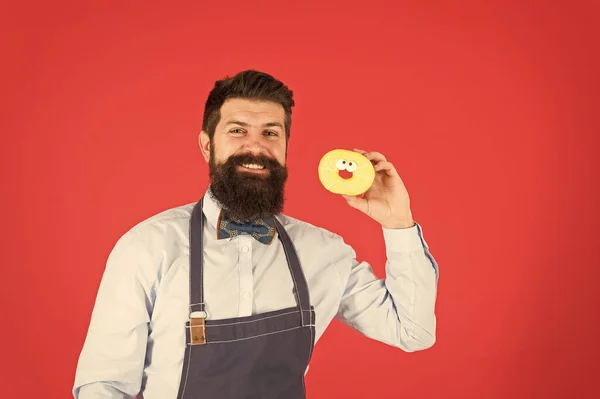 Homem barbudo e bem preparado com avental a vender donuts. Comida de donut. Produtos de panificação. Doces e bolos. Comida de plástico. Hipster barbudo padeiro segurar donuts. Come donut. Humor alegre. Calorias de donut. Donut vitrificado — Fotografia de Stock