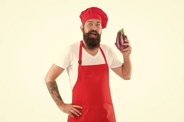 Vegetarian restaurant. Healthy cooking concept. Man with beard white background. Vegetarian recipe. Chef holds eggplant. Cook in uniform holds vegetables. Eat fresh food. Vegetarian chef cooking food