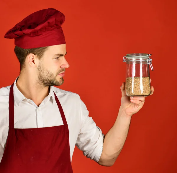 Man with beard holds jar with porridge on red background. — Stock Photo, Image