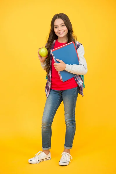 かわいいために良い食べ物を食べる。幸せな女の子はリンゴと本を保持します。脳の食物。学校のおやつだ。健康的な食事習慣。自然食品。精神的健康。認知的健康。学習と開発。子供の食事 — ストック写真