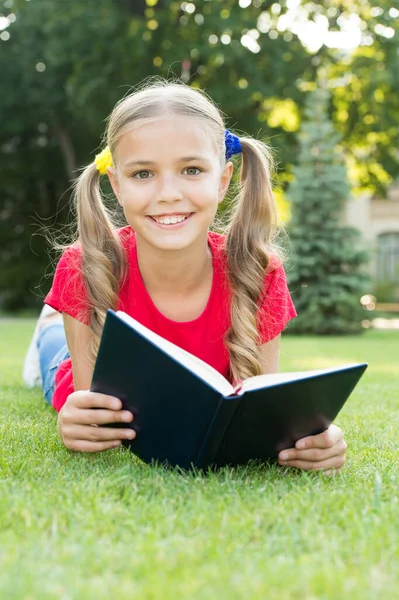 Kislány aranyos frizura olvasás könyv pihentető természet háttér, okos iskolás lány koncepció — Stock Fotó