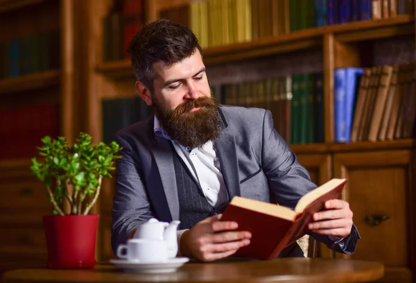 Retrato del hombre barbudo concentrado sosteniendo libro abierto y bebiendo té. —  Fotos de Stock