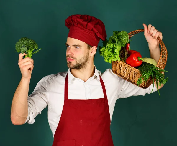 Chef en uniforme de borgoña mira brócoli una mano. —  Fotos de Stock