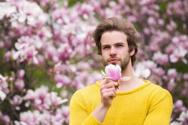 Sakallı, sarı süveterli, çiçekli bir maço.
