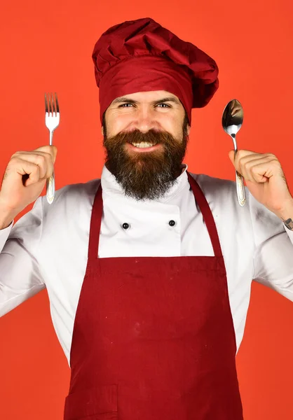 Cook with smiling face in burgundy uniform holds cutlery