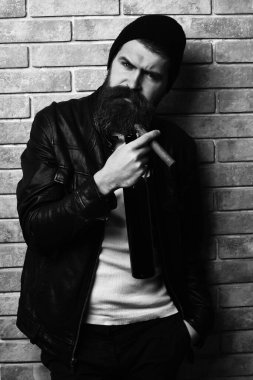 Beyaz sakallı, beyaz tenli hippi bej tuğlalı stüdyo arka planında puro içiyor.