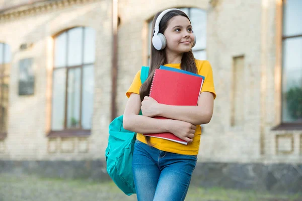 Její oblíbená melodie. Zpátky do školy. dospívající dívka poslouchat audio knihu. dítě se zápisníkem na školním dvoře. šťastný kluk držící složku. malá holka nosí sluchátka venku. školské vzdělání v moderním životě — Stock fotografie