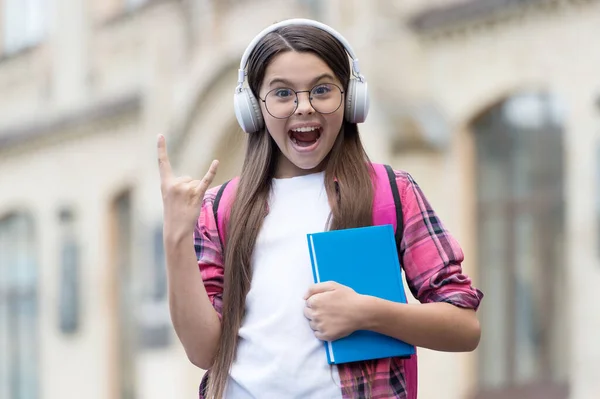 テクノロジー・ロックだ。幸せな子は角のサインをする。女の子はカジュアルなスタイルでヘッドフォンを着用します。英語学校。新しい技術だ。教育技術。外国語教育。オンラインコース。現代の生活 — ストック写真