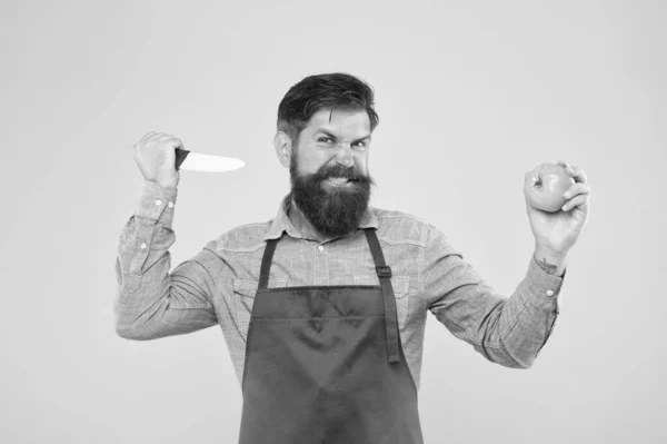 Biologisch voedsel. agressieve mannelijke chef werkt. volwassen kok gesneden groente. Een man in uniform in de keuken. vitamine dieet. Een man met een baard in een rood schort met gele tomaat. koken gezond en vers voedsel — Stockfoto