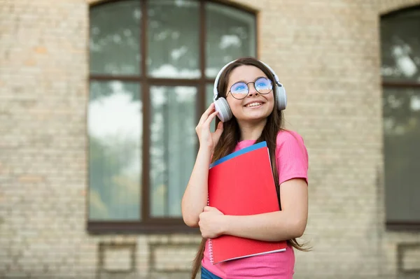 心情很好。快乐的童年小女孩戴着耳机。现代教育技术。快乐的女孩拿着文件夹。回学校去带着笔记本的快乐孩子儿童教育。听音乐 — 图库照片