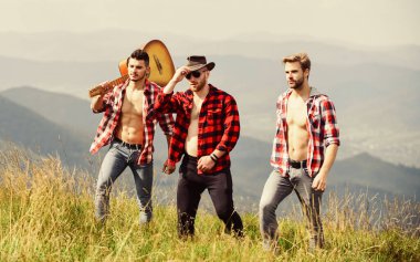 Güneşli bir günde gitarla yürüyüş yapan arkadaş canlısı adamlar. Turistler yürüyüş konsepti. Arkadaşlarla yürüyüş. Birlikte özgürlüğün tadını çıkarıyoruz. Kareli gömlekli bir grup genç dağın tepesinde birlikte yürüyorlar.