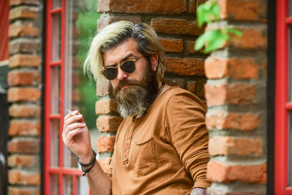 Een man die een sigaret rookt. Zakenman met een bril die sigaretten rookt op straat. Ga naar buiten voor rookpauze. Knappe stijlvolle man die buiten rookt in een stedelijke omgeving. hipster levensstijl — Stockfoto