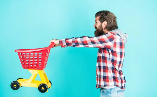 Sales assistant. empty toy trolley. really busy housekeeper. perfect husband. need shopping list. bearded man go shopping with toy empty shopping cart. customer pushing cart. buyer in supermarket