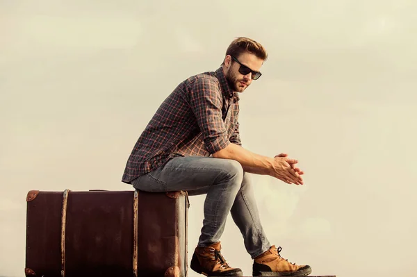 Abenteuer warten. Männermode. sieht so trendy aus. Macho-Mann mit unrasiertem Gesicht sitzt auf Tourtasche. Geschäftsmann mit Brille. Geschäftsreise. sexy Mann Himmel Hintergrund. Reisende warten auf den Flug. Umzug — Stockfoto