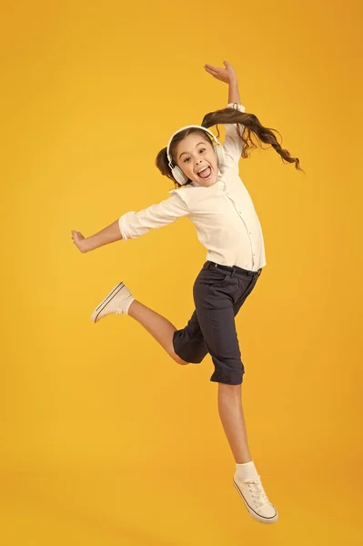 A melhor dançarina. Adorável pequeno dançarino se movendo para a música tocando em fones de ouvido. Pequena dançarina realizando salto de balé no fundo amarelo. Dançarina menina bonito dançando de volta para a escola de dança — Fotografia de Stock