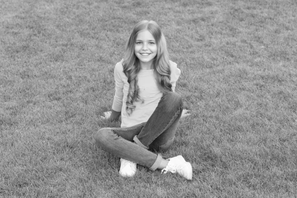 Menina feliz tem cabelo encaracolado longo. criança beleza e moda. menina adolescente após cabeleireiro. relaxar na grama verde. tempo de lazer primavera. infância feliz. criança com cabelo elegante. sorriso alegre — Fotografia de Stock