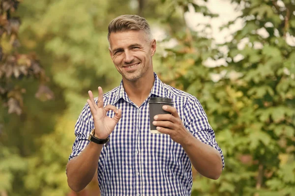 Capuchino perfecto. Propietario de plantación de café. Hombre bebiendo taza de papel de café. Un sorbo más. Beber café en el camino. Relájate y recarga. Guapo sonriente chico hold taza naturaleza fondo soleado día — Foto de Stock