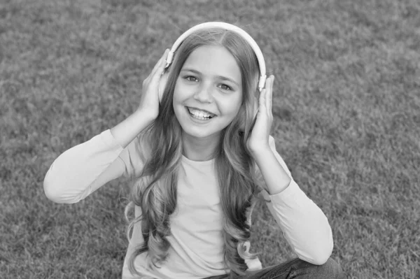 Pouca beleza relaxar no parque depois da escola. moda e beleza. feliz dia das crianças. férias de primavera. criança despreocupada na grama verde. A menina usa auscultadores. criança ouvindo música — Fotografia de Stock