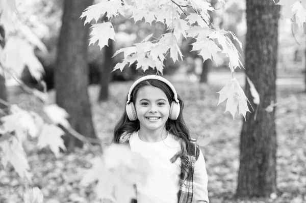 Melodia de outono. Menina feliz usar fones de ouvido na paisagem do outono. Criança bonito ouvir música em fones de ouvido estéreo. A criança pequena em fones de ouvido modernos gosta do dia de outono. Tecnologia de fones de ouvido — Fotografia de Stock