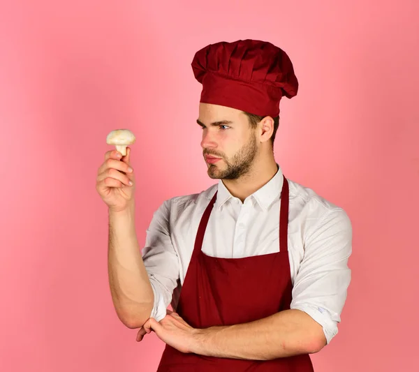 Man in cook hat and apron looks at ingredient.