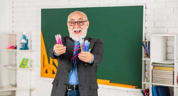 당신을 위해서요. 칠판이 있는 교실. 학교에서 물건을 쓰는 일. 남자는 여러 가지 사무 도구를 사용 한다. 교장 선생님은 화려 한 펜을 들고 있다. 색깔을 고르 세요. 행복 한 수염의 학교 선생님. 다시 학교로 — 스톡 사진
