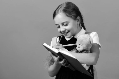 Kız oyuncak ayıyı tutuyor ve mavi defterine yazıyor.