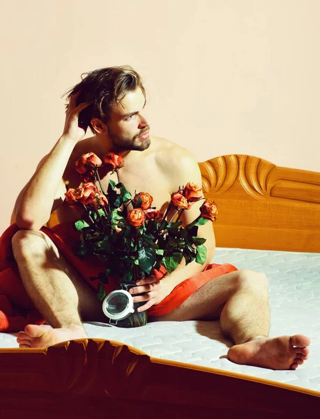 Macho barbudo con rosas en la cama bajo manta roja — Foto de Stock