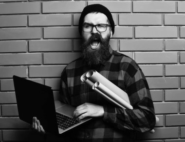 Kaba sakallı, beyaz tenli hippi elinde dizüstü bilgisayar ve el işi kâğıdı tutuyor.