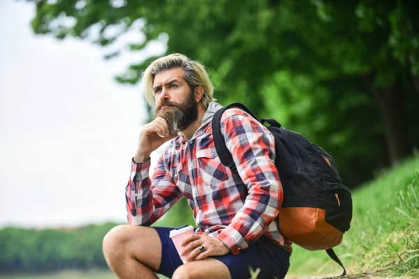 Inspired handsome hipster. Inspiration. Man outdoors with cup of coffee. Drinking hot coffee. Drink tea or coffee. Man with cup outdoors. Enjoying nature at riverside. Guy with backpack relaxing — Stock Photo, Image