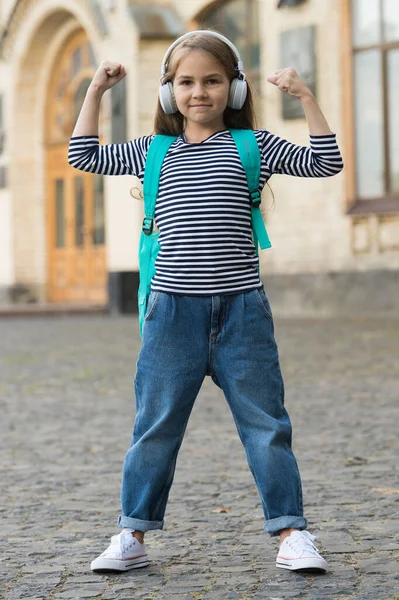 A beleza dá poder. Criança pequena flexionar braços ao ar livre. Poder feminino. Criança ouve música nos auscultadores. Música é poder. Nova tecnologia. Vida moderna. Estilo casual. Moda moda roupa — Fotografia de Stock